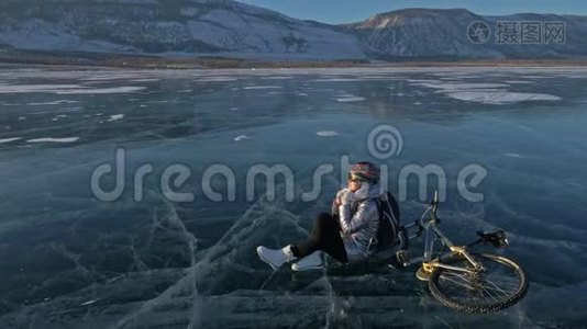 女人在冰上骑自行车。 女孩穿着银色羽绒服，自行车背包和头盔。 这就是视频
