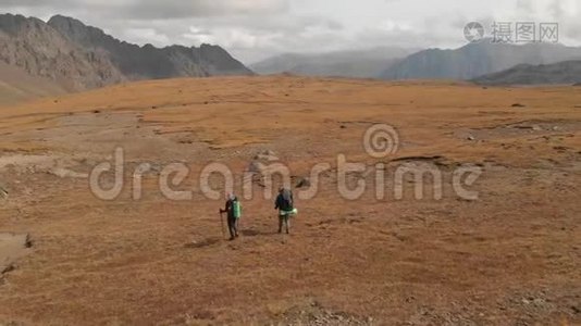 一对戴着帽子和太阳镜的大背包的旅行者男女在高山上漫步的鸟瞰图视频