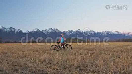 一个高加索儿童骑着自行车在麦田里行走。 女孩在美丽的白雪公主的背景下走着黑色橙色的自行车视频