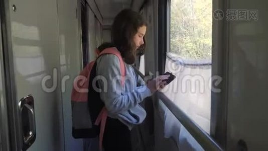 小女孩带着背包和智能手机在火车车厢里散步。 旅游运输铁路概念视频