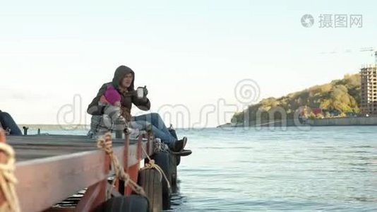 男人和女孩，父亲和女儿，坐在河港，喝茶，野餐，笑，穿着暖和的衣服视频