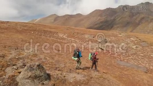 一对戴着帽子和太阳镜的大背包的旅行者男女在高山上漫步的鸟瞰图视频