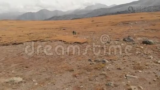 一对戴着帽子和太阳镜的大背包的旅行者男女在高山上漫步的鸟瞰图视频