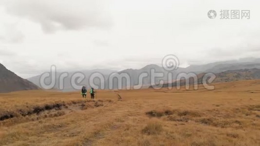 一对戴着帽子和太阳镜的大背包的旅行者男女在高山上漫步的鸟瞰图视频