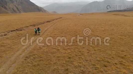 一对戴着帽子和太阳镜的大背包的旅行者男女在高山上漫步的鸟瞰图视频