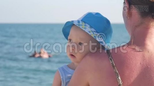 年轻的母亲把儿子抱在海边的怀里。视频