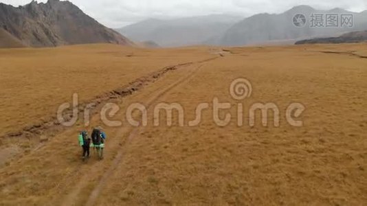 一对戴着帽子和太阳镜的大背包的旅行者男女在高山上漫步的鸟瞰图视频