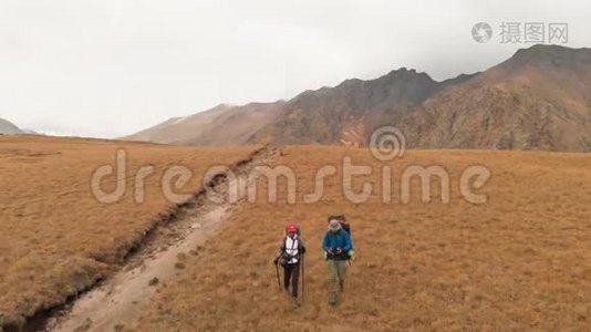 一对戴着帽子和太阳镜的大背包的旅行者男女在高山上漫步的鸟瞰图视频