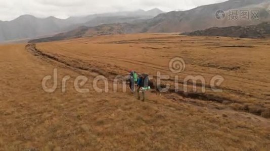 一对戴着帽子和太阳镜的大背包的旅行者男女在高山上漫步的鸟瞰图视频