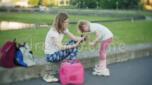 妈妈帮女儿戴上头盔和防护用具，在公园里溜冰。 女人帮助女孩视频