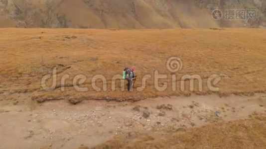 一对戴着帽子和太阳镜的大背包的旅行者男女在高山上漫步的鸟瞰图视频