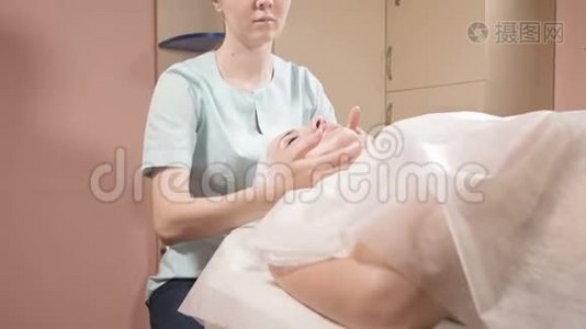 戴着面具和手套的女美容师给一个有魅力的女人做一个有益健康的面部按摩。 新一代视频