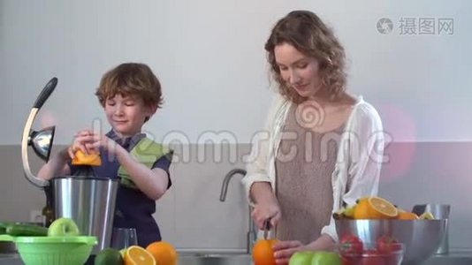 年轻的白种人母亲和孩子在厨房用电榨汁机制作鲜橙果汁视频