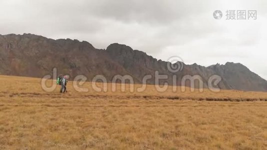 一对戴着帽子和太阳镜的大背包的旅行者男女在高山上漫步的鸟瞰图视频
