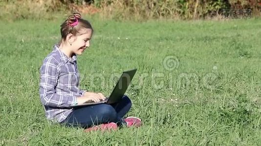 小女孩坐在草地上玩手提电脑视频