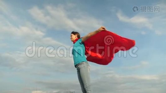 美丽的女孩超级英雄穿着红色斗篷站在田野上，斗篷随风飘扬。 慢动作。 女孩的梦想视频
