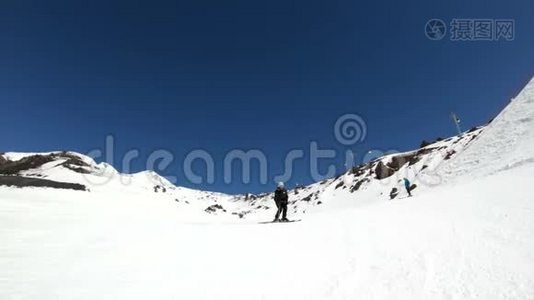 阳光明媚的一天，一个身穿黑色装备、戴着滑雪杆的白色头盔的宽角男滑雪者骑在雪坡上视频