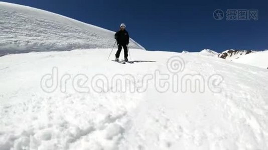 阳光明媚的一天，一个身穿黑色装备、戴着滑雪杆的白色头盔的宽角男滑雪者骑在雪坡上视频