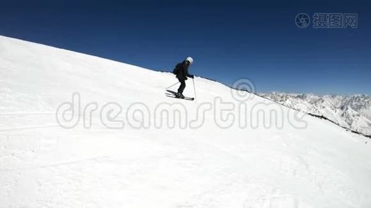 阳光明媚的一天，一个身穿黑色装备、戴着滑雪杆的白色头盔的宽角男滑雪者骑在雪坡上视频