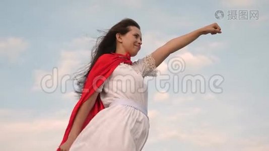 美丽的超级英雄女孩站在一片红色斗篷的田野上，斗篷在风中飘扬。 女孩梦想成为一个视频
