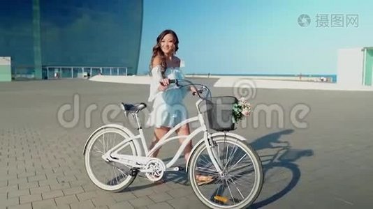 穿着蓝色连衣裙的亚洲模特骑着白色自行车在海上露台上视频