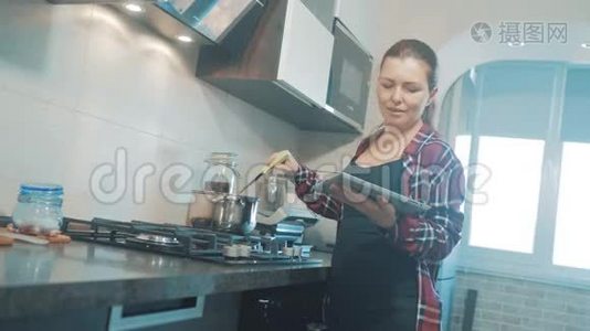 女人在厨房煮汤，防止锅中的水，看看数字平板上的食谱。 妇女视频