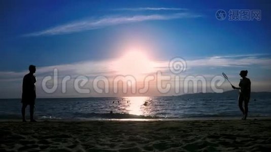 剪影。 人们在日落时在海滩上打羽毛球。视频
