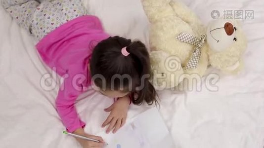 可爱的小女孩躺在床上画画。视频