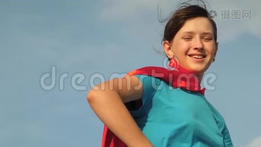 女孩梦想成为超级英雄。 美丽的女孩超级英雄穿着红色斗篷站在田野上，斗篷随风飘扬视频