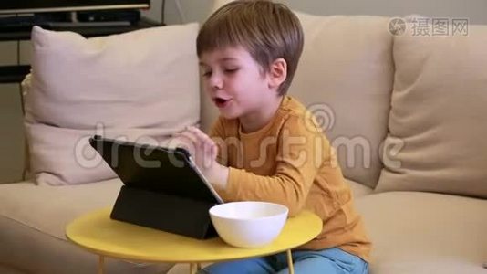 孩子在家里的床上使用平板电脑。 沙发上可爱的男孩正在看卡通，玩游戏，从笔记本电脑上学习。 教育、娱乐视频