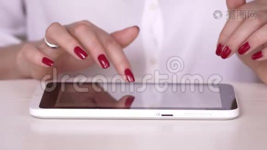 那个女人在平板电脑上工作。 做红色指甲的女商人。 穿白衬衫的女人看着有关视频