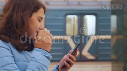 十几岁的女孩带着智能手机和耳机等待地铁，很多人聚集在地下。 地下地铁公司视频