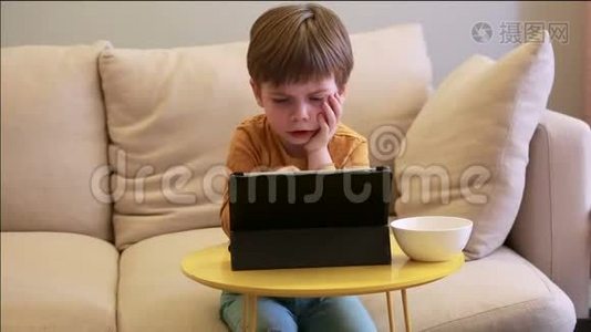 孩子在家里的床上使用平板电脑。 沙发上可爱的男孩正在看卡通，玩游戏，从笔记本电脑上学习。 教育、娱乐视频
