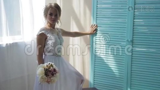 美丽的金发碧眼，穿着一件白色的新娘礼服，靠近一扇窗户，放着一束鲜花视频