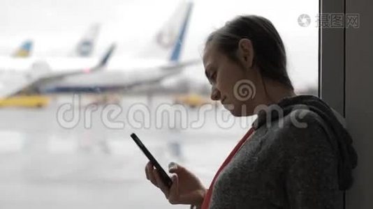 年轻女子在机场使用智能手机，背景是飞机视频