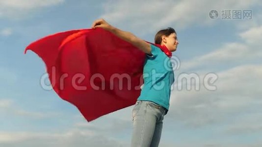 美丽的女孩超级英雄穿着红色斗篷站在田野上，斗篷随风飘扬。 慢动作。 女孩的梦想视频