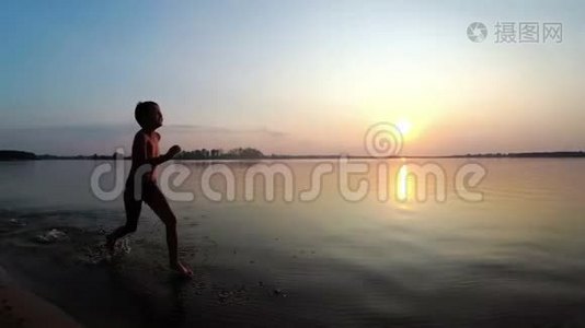 日落时，快乐的孩子沿着海滩奔跑。 慢动作视频