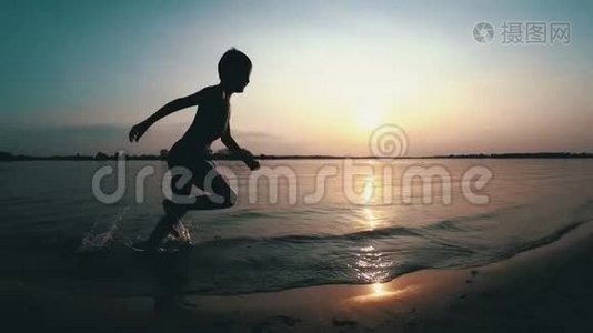 日落时，快乐的孩子沿着海滩奔跑。 慢动作视频