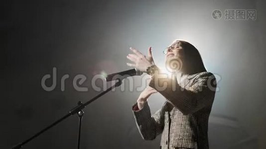 这位女金融教练从舞台上与观众进行情感手势交谈。 太多匿名者视频