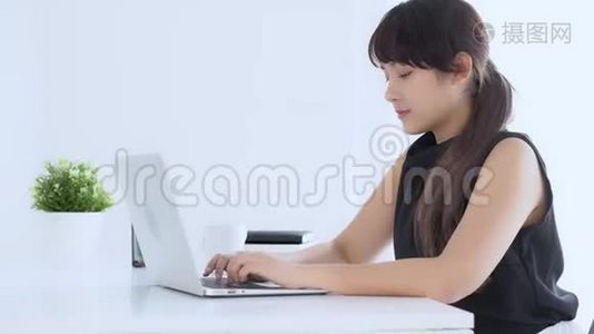 美丽的年轻自由职业亚洲女性微笑着在办公桌办公室的笔记本电脑上工作和打字视频