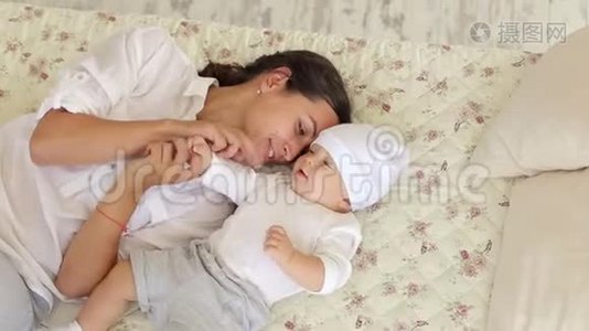 年轻快乐的妈妈正在床上卧室里和一个新生儿玩耍。视频
