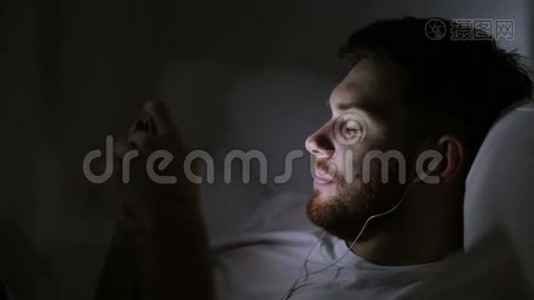 有智能手机和耳机的男人在床上过夜视频