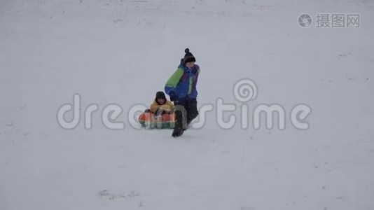 冬天的雪乐趣。 孩子们从滑梯上骑着一根管子。视频