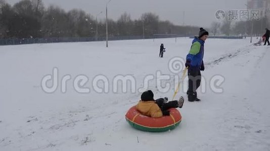 冬天的雪乐趣。 孩子们从滑梯上骑着一根管子。视频