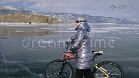 女人在冰上骑着自行车走着。 女孩穿着银色的羽绒服，背包和头盔。 冰冰视频