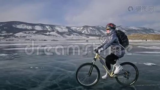 女人在冰上骑自行车。 女孩穿着银色羽绒服，自行车背包和头盔。 冰冰视频