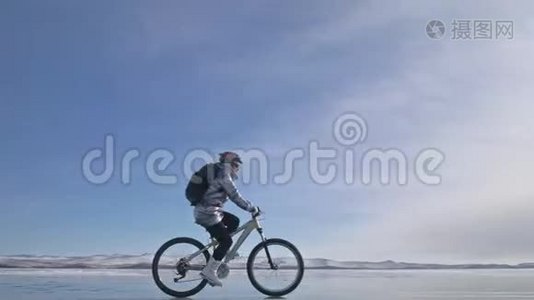 女人在冰上骑自行车。 女孩穿着银色羽绒服，自行车背包和头盔。 冰冰视频