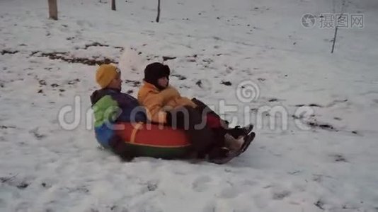 冬天的雪乐趣。 孩子们从滑梯上骑着一根管子。视频