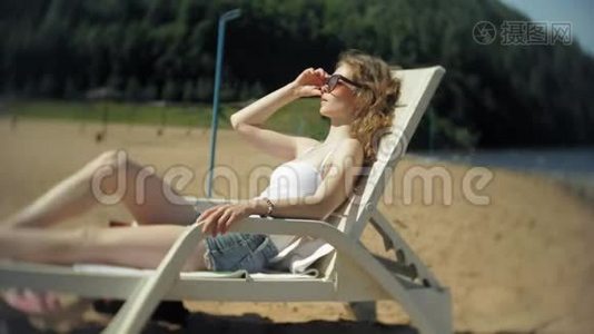 穿白色比基尼的年轻女孩躺在沙滩上的躺椅上晒太阳视频