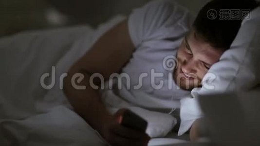 有智能手机和耳机的男人在床上过夜视频